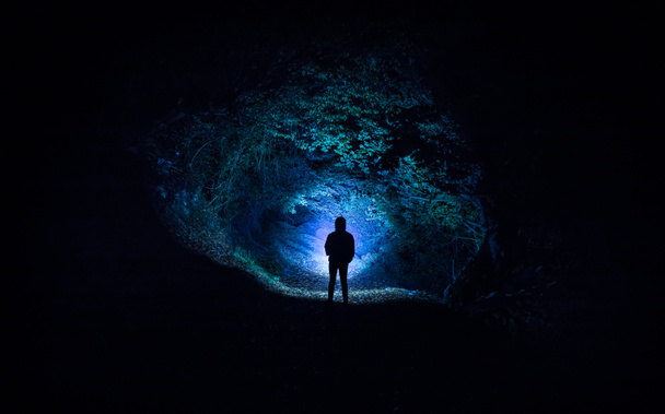Siluetti henkilö seisoo pimeässä metsässä valoa. Kauhu halloween käsite. outo siluetti pimeässä aavemaisessa metsässä yöllä - Valokuva, kuva