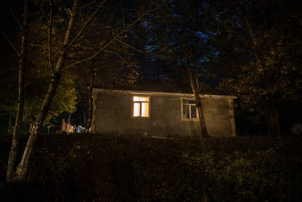 夜に森の中に幽霊と古い家や放棄された幽霊の恐怖の家。死んだ木の森の中の古い神秘的な建物。本物のライトだ。ホラーハロウィンのコンセプト - 写真・画像