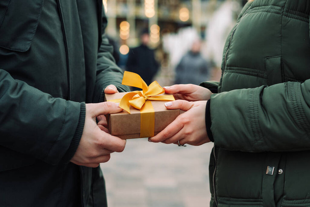 Mani di una coppia con un regalo. L'uomo fa un piccolo regalo con un nastro giallo alla sua ragazza per strada. Una donna riceve un regalo dal suo ragazzo. Giorno di San Valentino e concetto di Natale - Foto, immagini