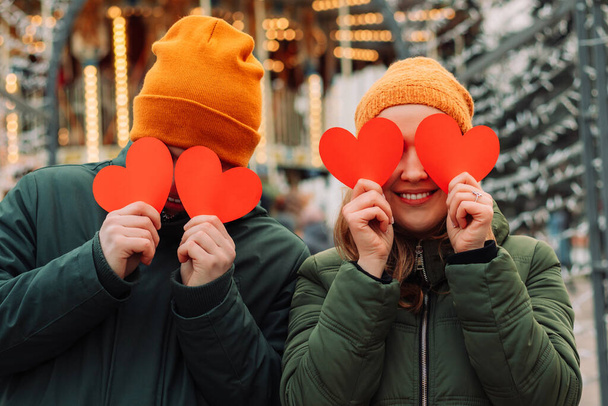 Joven pareja feliz divirtiéndose al aire libre con corazones de papel rojo en temporada de invierno. Un niño y una niña se aman y pasan tiempo juntos antes del día de San Valentín. Vacaciones y concepto de Navidad - Foto, Imagen