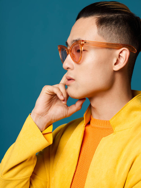 Side view of a young man in sunglasses and a yellow jacket on a blue background - Foto, imagen