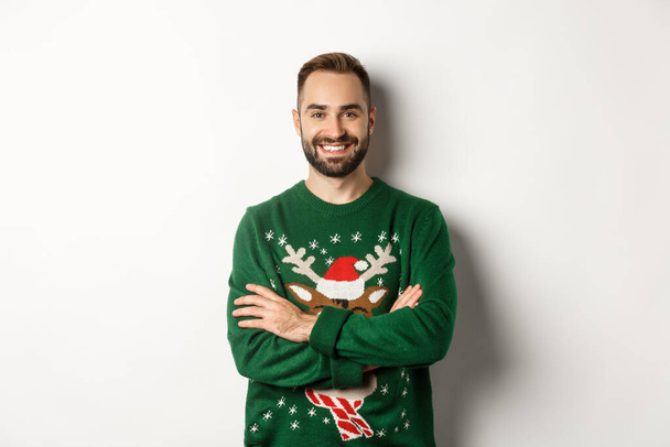 New Year party and winter holidays concept. Happy bearded man in funny christmas sweater standing against white background - Foto, Bild