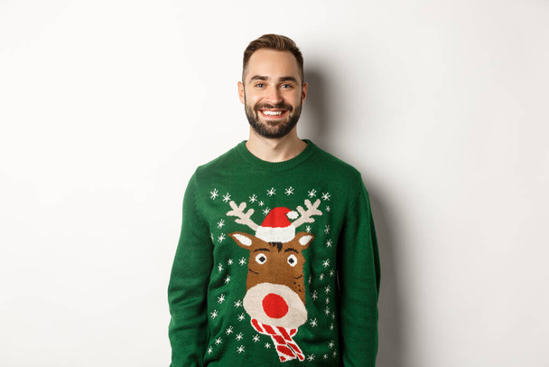New Year party and winter holidays concept. Happy bearded man in funny christmas sweater standing against white background - 写真・画像