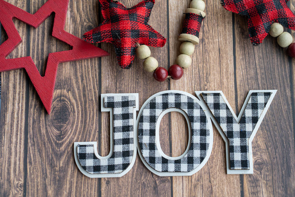 Black and white joy plaid phrase on a wood background with red stars, useful for Christmas projects - Photo, image