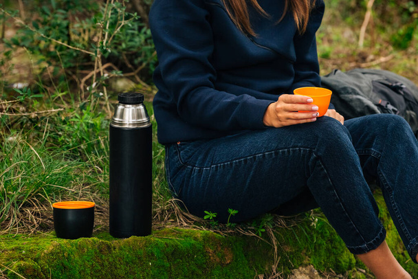 Woman drinking tea from thermos during hike outdoors. Refreshment during hiking in the woods - Zdjęcie, obraz