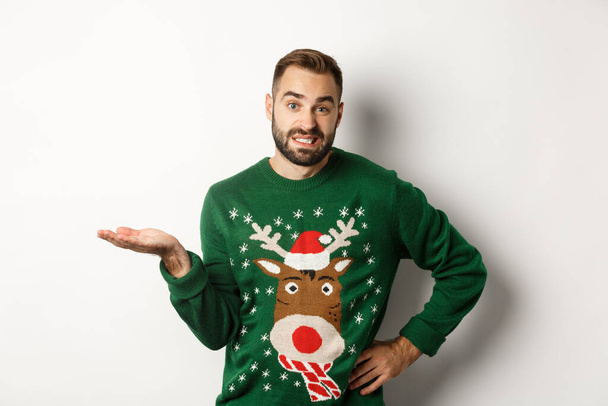 New Year, holidays and celebration. Confused bearded guy in funny sweater, shrugging and looking clueless, dont know, looking awkward, standing over white background - Foto, Imagem