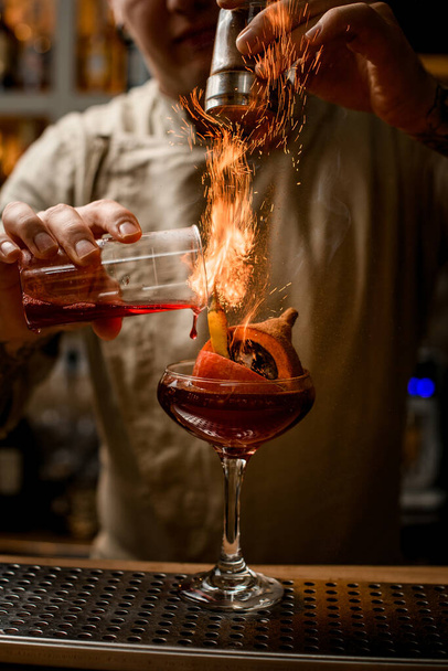 male barman add ingredients to glass with pumpkin and pepper inside and makes fire over it - Foto, Bild