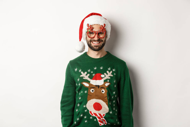 Karácsonyi ünnepek, ünnepi fogalom. Boldog ember a Mikulás kalap és vicces party szemüveg álló ellen fehér háttér - Fotó, kép