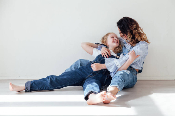 Η μαμά μελαχρινή και η κόρη ξανθιά με τζιν κάθονται στο πάτωμα. - Φωτογραφία, εικόνα