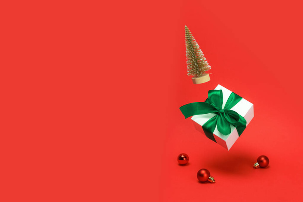 Feliz escena navideña. Árbol dorado de invierno, caja de regalo blanca con lazo verde que cae con bolas rojas y luces brillantes en la decoración de Navidad sobre fondo rojizo. Fondo de Navidad con espacio para texto. - Foto, imagen