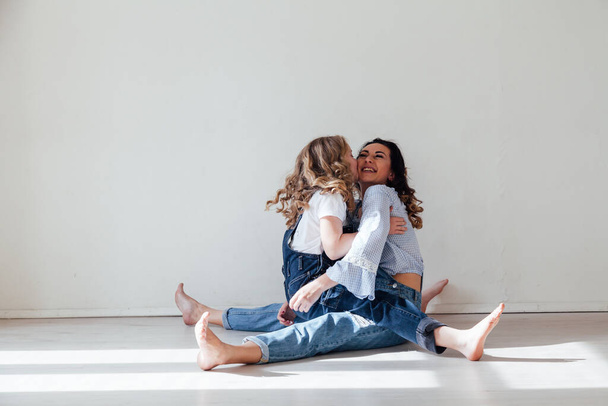 Moeder brunette en dochter blond in jeans zitten op de vloer - Foto, afbeelding