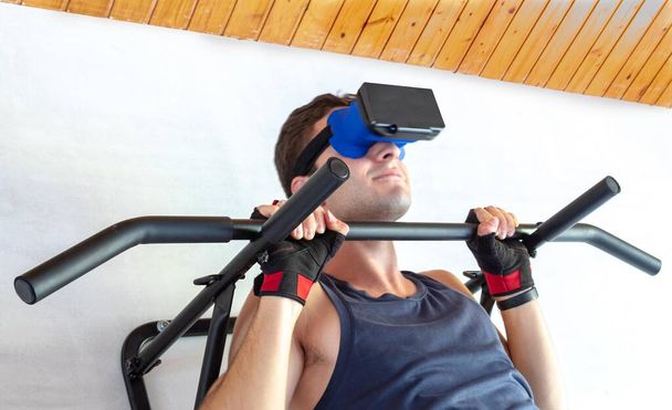 young man smiling enjoying virtual reality while doing sit-ups on a fixed drawbar at home - Foto, afbeelding