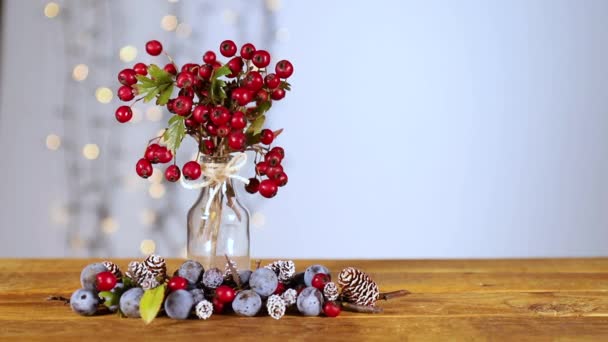 クリスマスを陽気でベリーにしましょう!明るい雰囲気のための点滅ライト。木のテーブルの上のホリーベリー、冬の色と小さな松の実は、彼らの魅力的な自然なタッチで魂を落ち着かせます. - 映像、動画