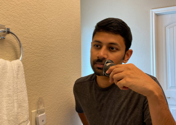 Aynaya bakan ve tıraş makinesi kullanan bir adamın yakın görüntüsü. - Fotoğraf, Görsel