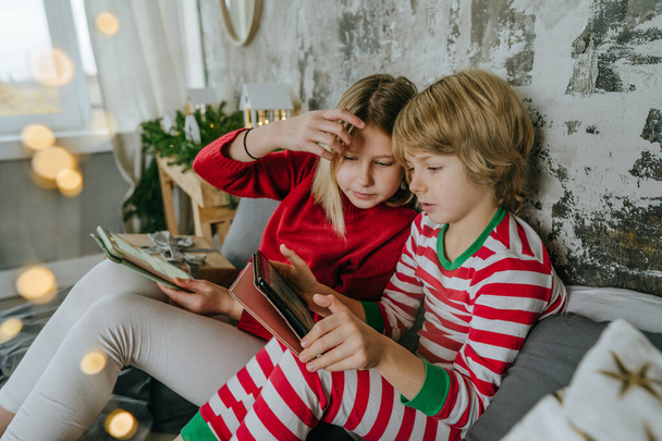 Αγόρι και κορίτσι χρησιμοποιούν ταμπλέτες για βιντεοκλήση ή παιχνίδια την περίοδο των Χριστουγέννων. Επιλεκτική εστίαση. - Φωτογραφία, εικόνα
