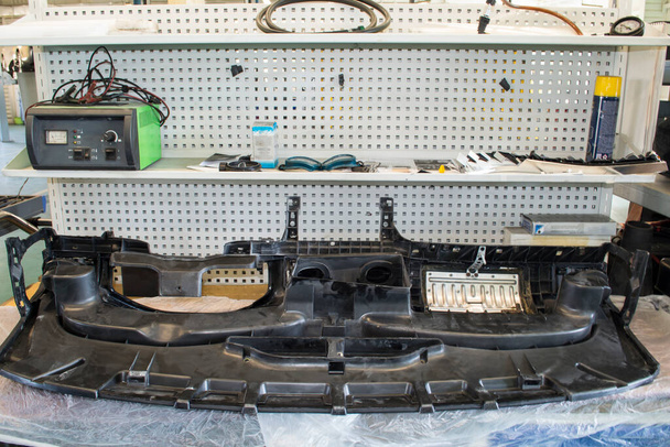 Un tablero invertido del coche miente en el banco de trabajo de un electricista en un taller de reparación auto - Foto, imagen