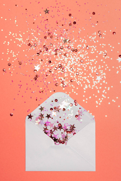 Sparkling confetti scattered from envelope on coral background. - Photo, Image