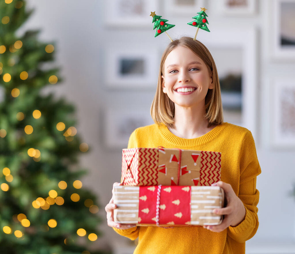 Noel için hediye paketlenmiş mutlu genç bir kadın evdeki kameraya gülümsüyor. - Fotoğraf, Görsel