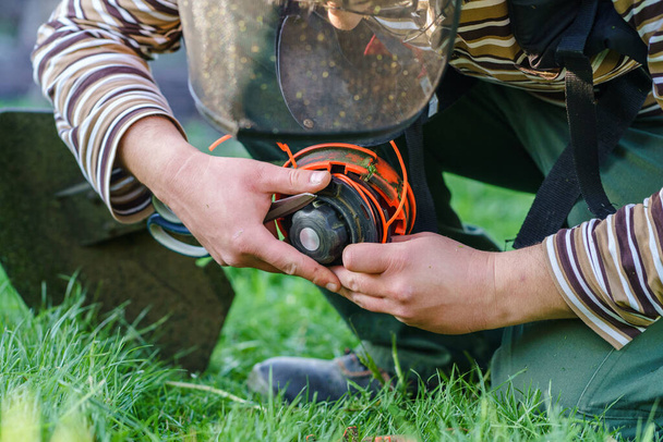 Close up on string trimmer head unknown caucasian man holding and repairing weed cutter replacing parts replacement in day on the field farmer or gardener - Photo, Image