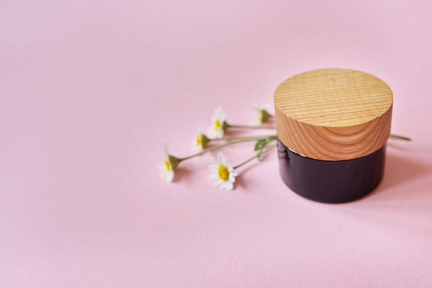Cosmetic product in bottle with chamomile flowers on pink background - Valokuva, kuva
