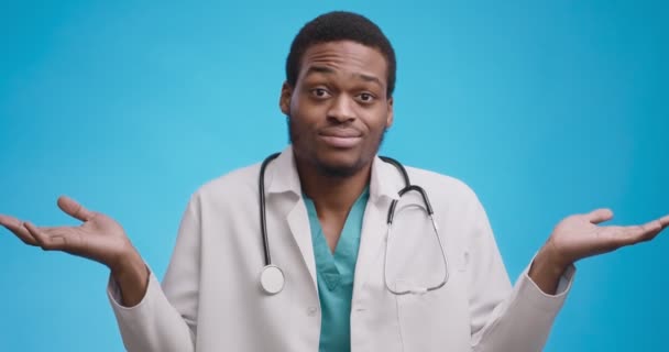Retrato del inseguro médico afroamericano en brazos médicos blancos encogiéndose de hombros, haciendo que no sepa gesto - Metraje, vídeo