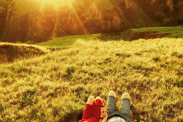 guy and girl lie on the grass, top view. Romantic date at sunset in a beautiful quarry with hills at sunse - Photo, Image