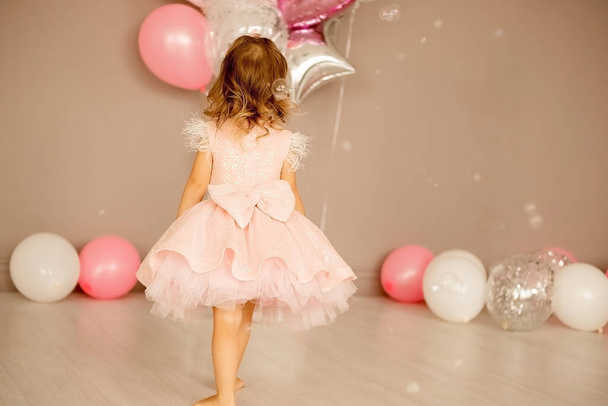 little girl in a bright room in a smart pink dress. balloons lie on the floor, concept of childhood, birthda - Photo, Image