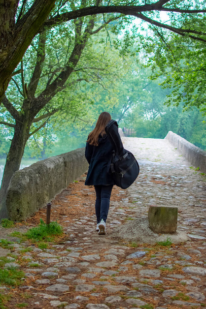 Молодая девушка носит гитарную сумку во время прогулки в тошноте - Фото, изображение