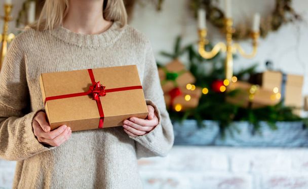 Woman hold gift box near Christmas decorated fireplace at home  - Valokuva, kuva