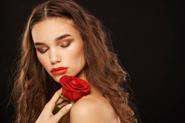 femme avec une rose rouge sur un fond sombre cheveux longs maquillage lèvres rouges - Photo, image