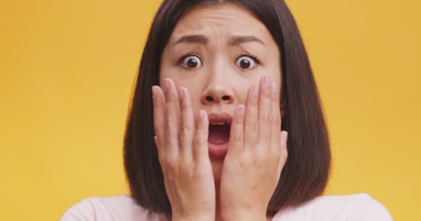 Joven sorprendido mujer asiática cerrando la boca en asombro, mirando preocupado y aturdido, fondo de estudio naranja - Imágenes, Vídeo