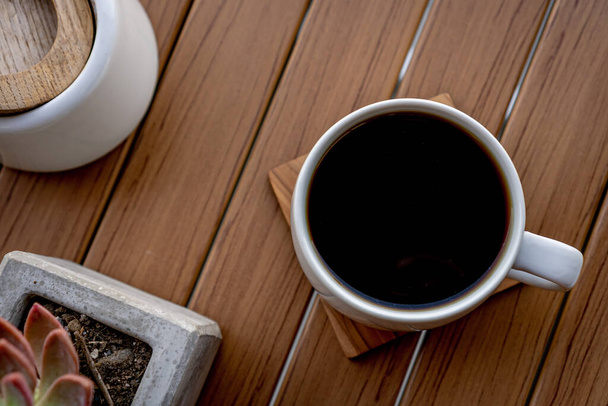 Bílý šálek černé kávy na dřevěném podstavci na dřevěném stole. - Fotografie, Obrázek