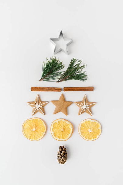 Christmas, winter, new year composition. Creative fir tree made of fir tree branches, pine cone, cinnamon sticks, dried oranges, gingerbread on white background. Flat lay, top view - Photo, image