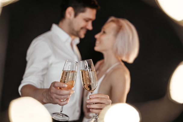Beautiful happy couple young family in evening dresses with glasses of champagne on dark background, selective focus - Foto, imagen