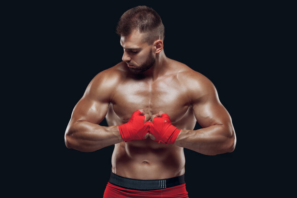 Front view of a sporty man in boxing gloves practicing fighting techniques isolated on black background - Φωτογραφία, εικόνα