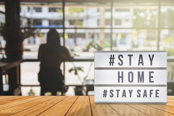 Signo de caja de luz con etiqueta de texto # STAY HOME y # STAY SAFE con sombra de mujer, fondo borroso de cafetería. COVID-19. Quedarse en casa guardar concepto. - Foto, imagen