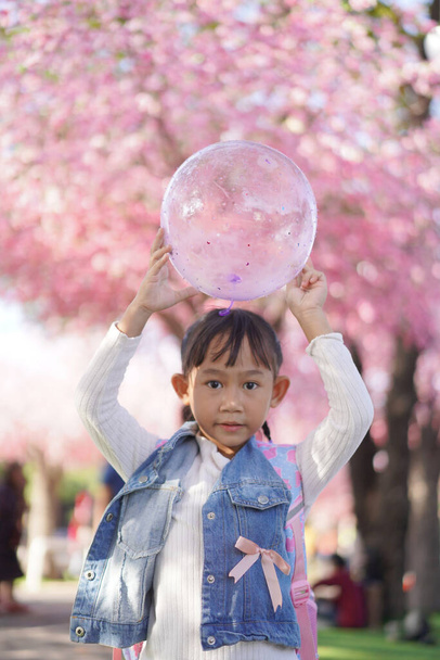 Asian little girl in garden under the blossom sakura tree background  - Fotó, kép
