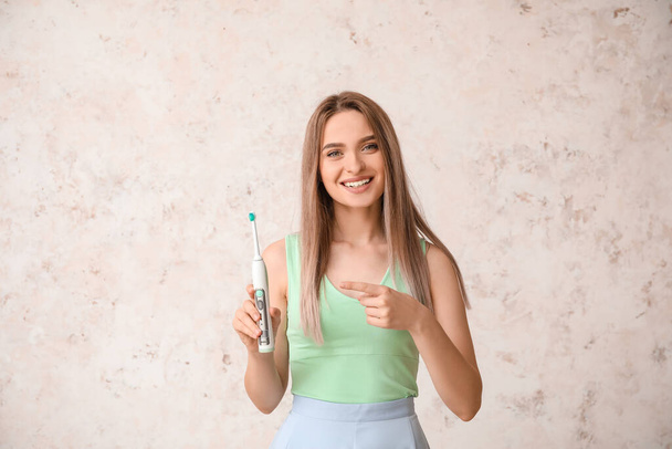 Молода жінка з електричною зубною щіткою на світлому фоні
 - Фото, зображення