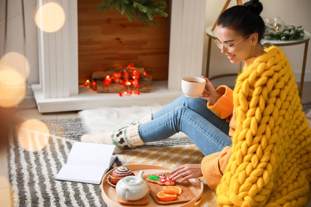 Belle jeune femme avec livre de lecture à carreaux chauds et boire du thé à la maison - Photo, image