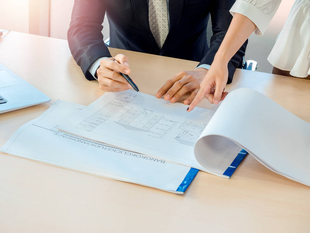 Woman hand pointing blueprint on wooden desk in office with engineer in suit using pen pointing, too. Businessman and woman working together, investigate, design, analyze problems and fix concept. - Fotó, kép