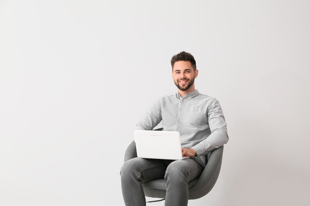 Man psycholoog met laptop zittend in fauteuil op lichte achtergrond - Foto, afbeelding