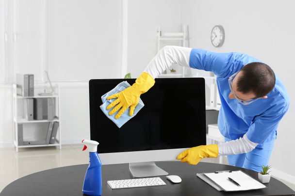 Male janitor cleaning computer in office - 写真・画像