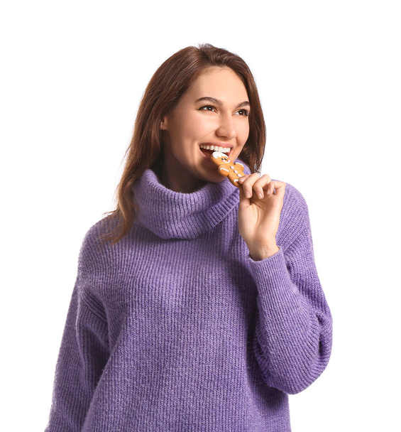 Beautiful young woman eating tasty gingerbread cookie on white background - Foto, Imagem