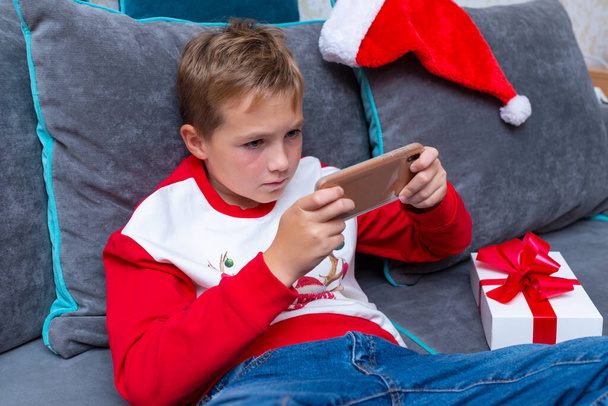 Ελκυστικό παιδί αγόρι χρησιμοποιώντας smartphone για τις διακοπές των Χριστουγέννων λευκό δώρο για τη φωτογραφία μας στο σπίτι.about view. - Φωτογραφία, εικόνα
