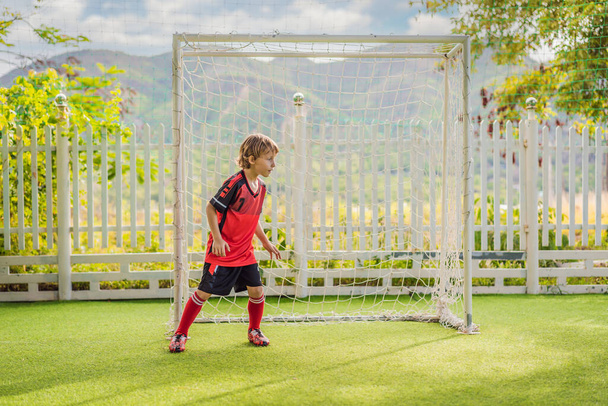 Little cute kid boy in red football uniform playing soccer, football on field, outdoors. Active child making sports with kids or father, Smiling happy boy having fun in summer - Foto, Imagen