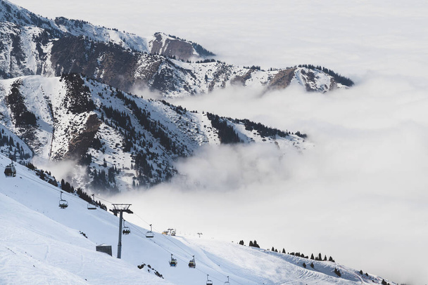 Ośrodek narciarski w górach Cloudy Tian Shan we mgle. Wyciąg narciarski na stoku. Koncepcja urlopu Almaty tle. - Zdjęcie, obraz