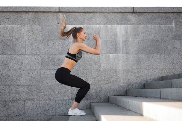 Urban sporty woman training. Female athlete doing squat jumps on urban stairs. Fitness motivation Healthy lifestyle concept - Photo, image