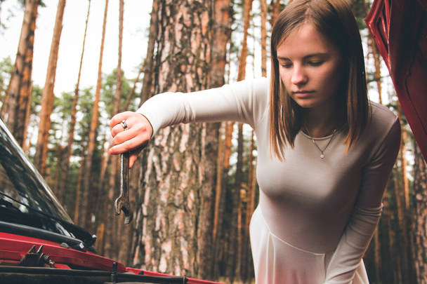 Chernigov, Ukraine - November 10, 2020: A girl in a white wedding dress holds a wrench in her hands. Vaz 2101. Red retro car in the forest - Fotó, kép