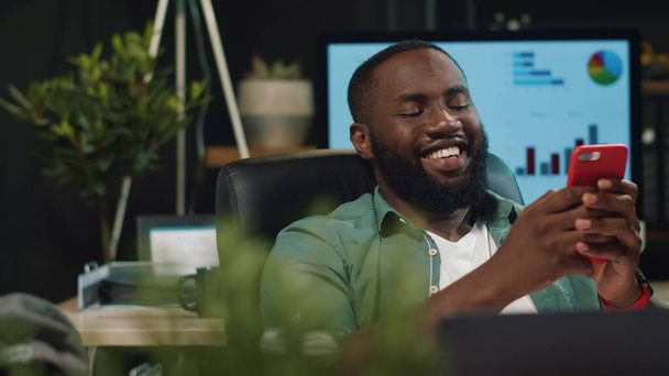 Nahaufnahme freudiger Afro-Geschäftsmann tippt Nachricht auf Smartphone im Hipster-Büro - Foto, Bild
