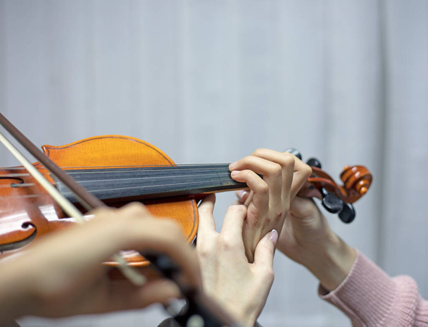 segítve a tanárt abban, hogy helyesen tartsa a kezét a hegedűn, gyermekkezeket helyezve el hegedülés közben - Fotó, kép